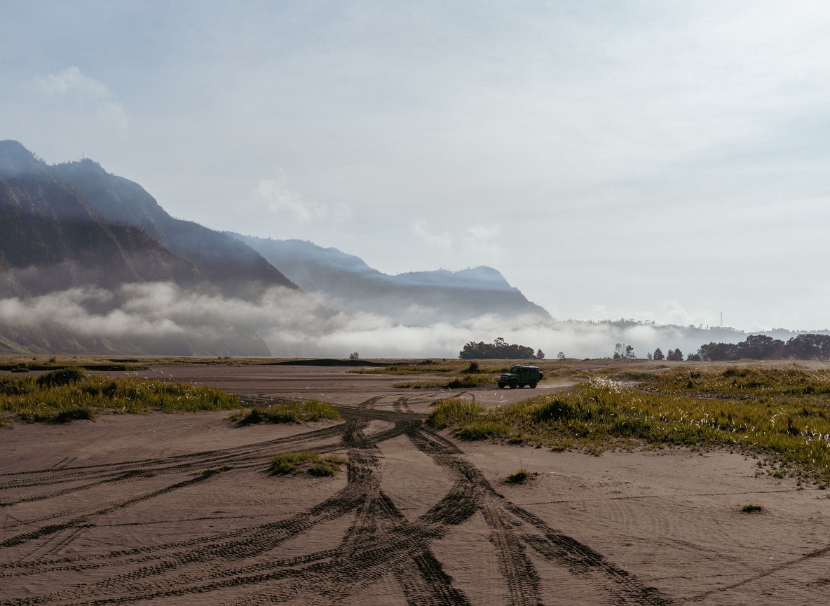 a private safari vehicle parked on a Mara concession track at sunset with two guests watching a lion in the distance