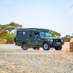 A safari Land Cruiser with guests aboard driving through acacia bushland in the Maasai Mara, Kenya