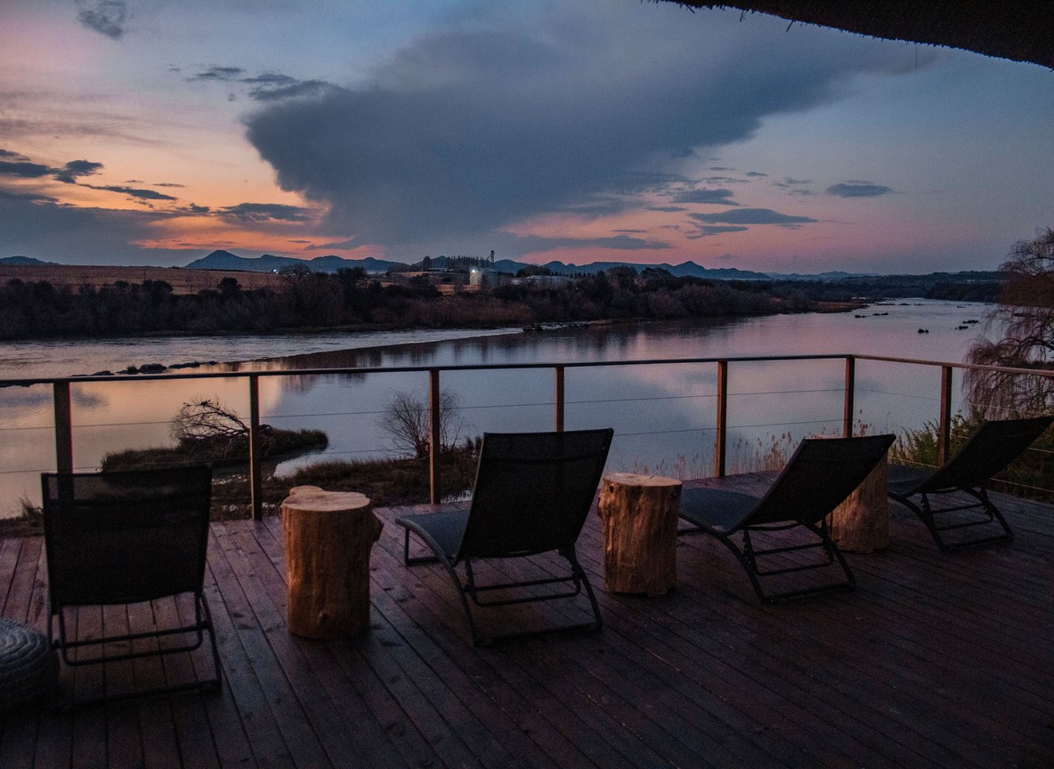 Empty wooden deck chairs overlooking a river at dusk, private conservancy camp setting