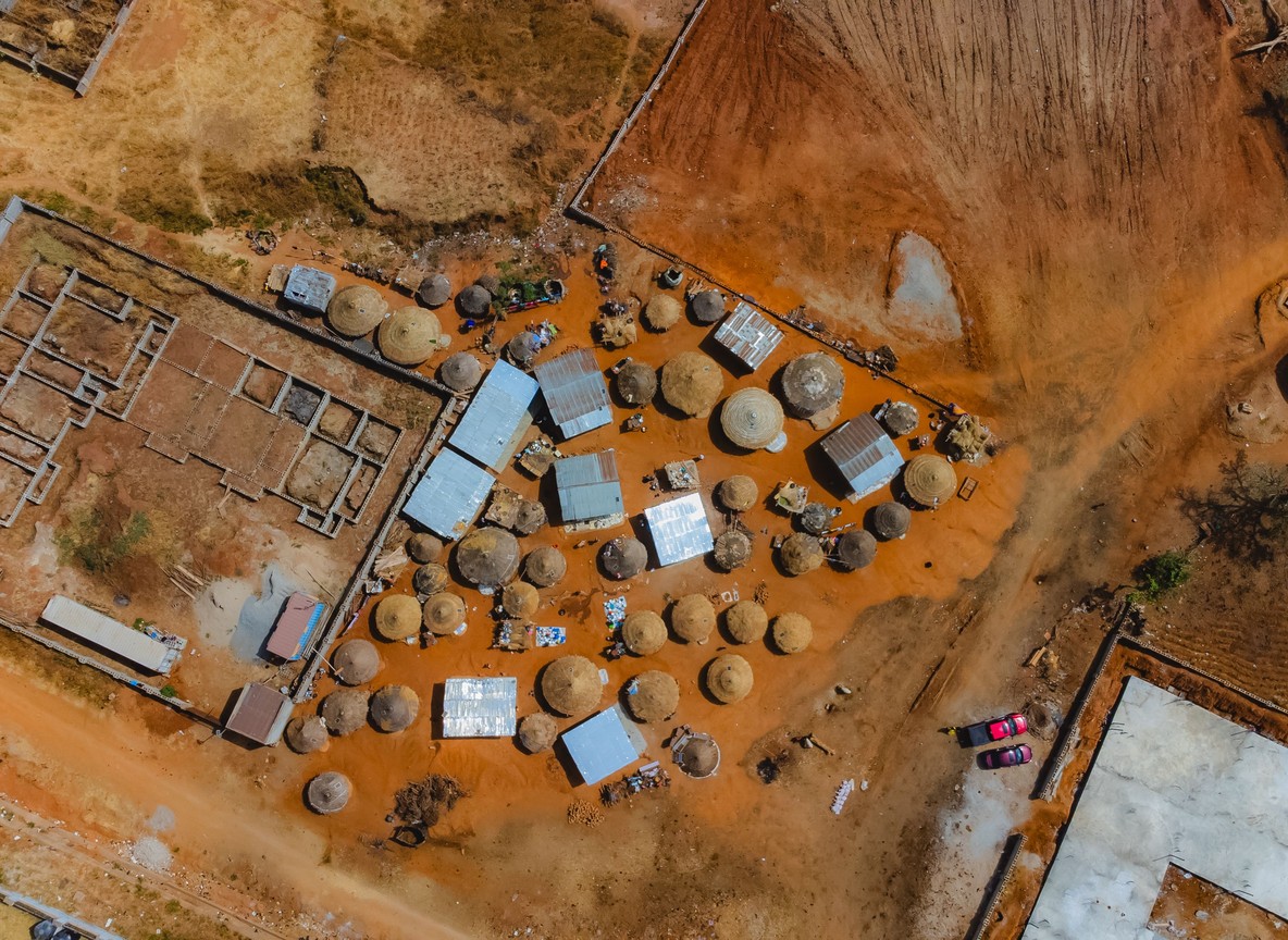 Maasai children and adults inside a manyatta homestead compound made of mud and stick houses, cattle enclosure visible, natural daylight