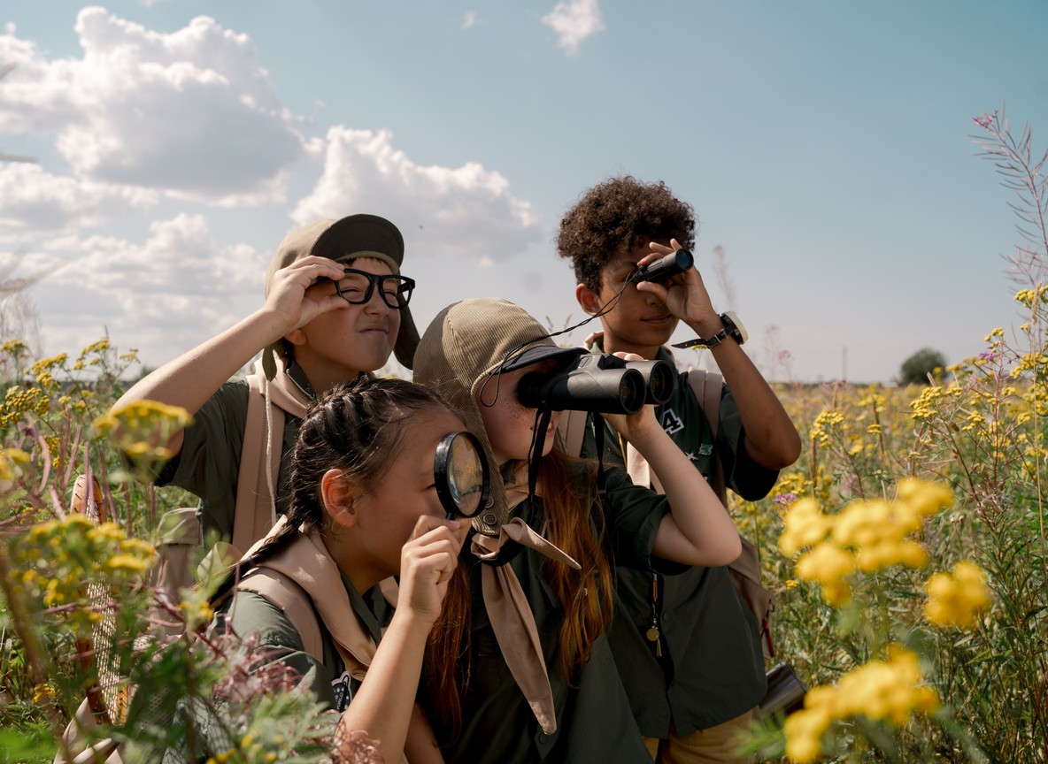 A young child looking through binoculars at giraffes near a safari vehicle in Tsavo East National Park