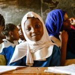 African schoolgirls in uniform sitting together in a rural classroom, the kind of setting the menstrual health program works to keep girls attending
