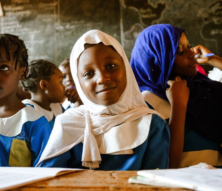 African schoolgirls in uniform sitting together in a rural classroom, the kind of setting the menstrual health program works to keep girls attending
