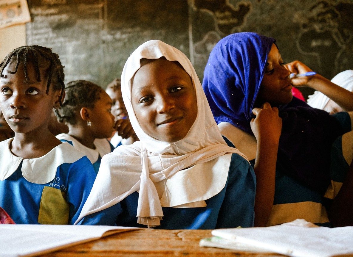 African schoolgirls in uniform sitting together in a rural classroom, the kind of setting the menstrual health program works to keep girls attending