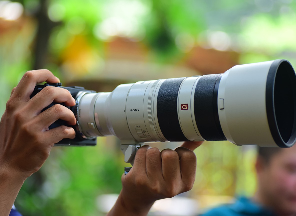 A safari photographer holding a large telephoto lens, close-up detail of camera gear used on guided workshops
