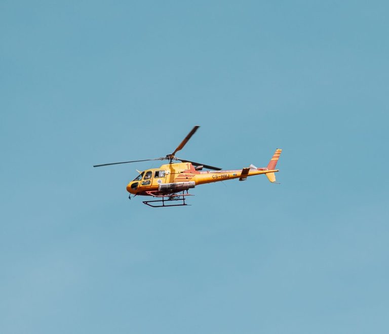 A helicopter flying low over the Masai Mara grasslands at golden hour with wildebeest herds visible below