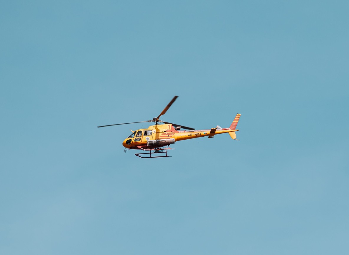 A helicopter flying low over the Masai Mara grasslands at golden hour with wildebeest herds visible below