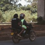 a solo woman traveler with a daypack walking confidently through a quiet, leafy Nairobi neighborhood street in daylight