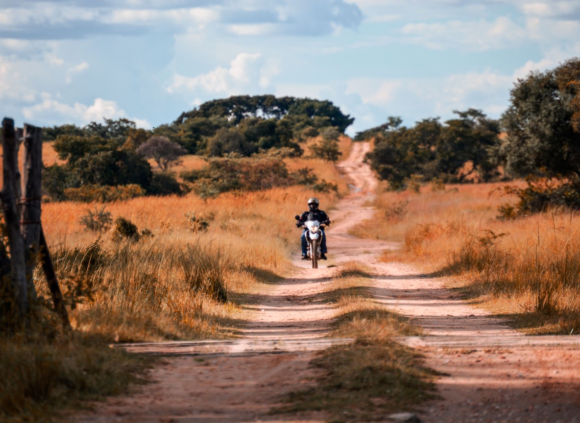 A rider on a dirt track winding through open grassland near the Kenya-Tanzania border corridor, the kind of remote stretch overland travelers cover between the Mara and Isebania
