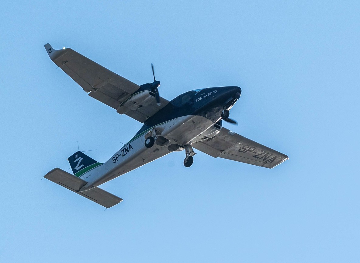 Small twin-engine safari charter aircraft banking in flight over a regional airstrip