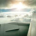 a view from a plane window of the engine and wing above clouds with sunlight breaking through