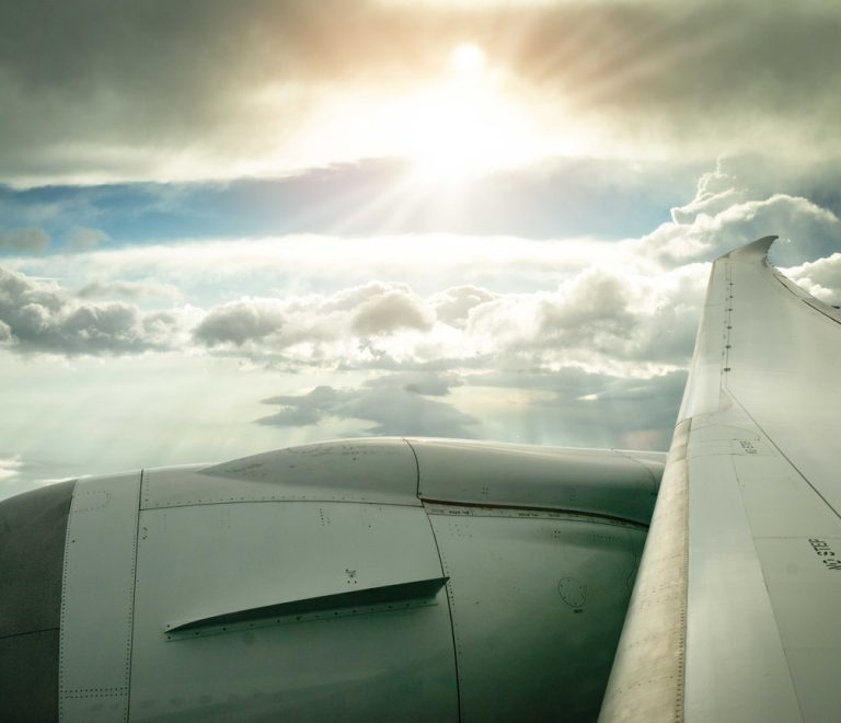 a view from a plane window of the engine and wing above clouds with sunlight breaking through
