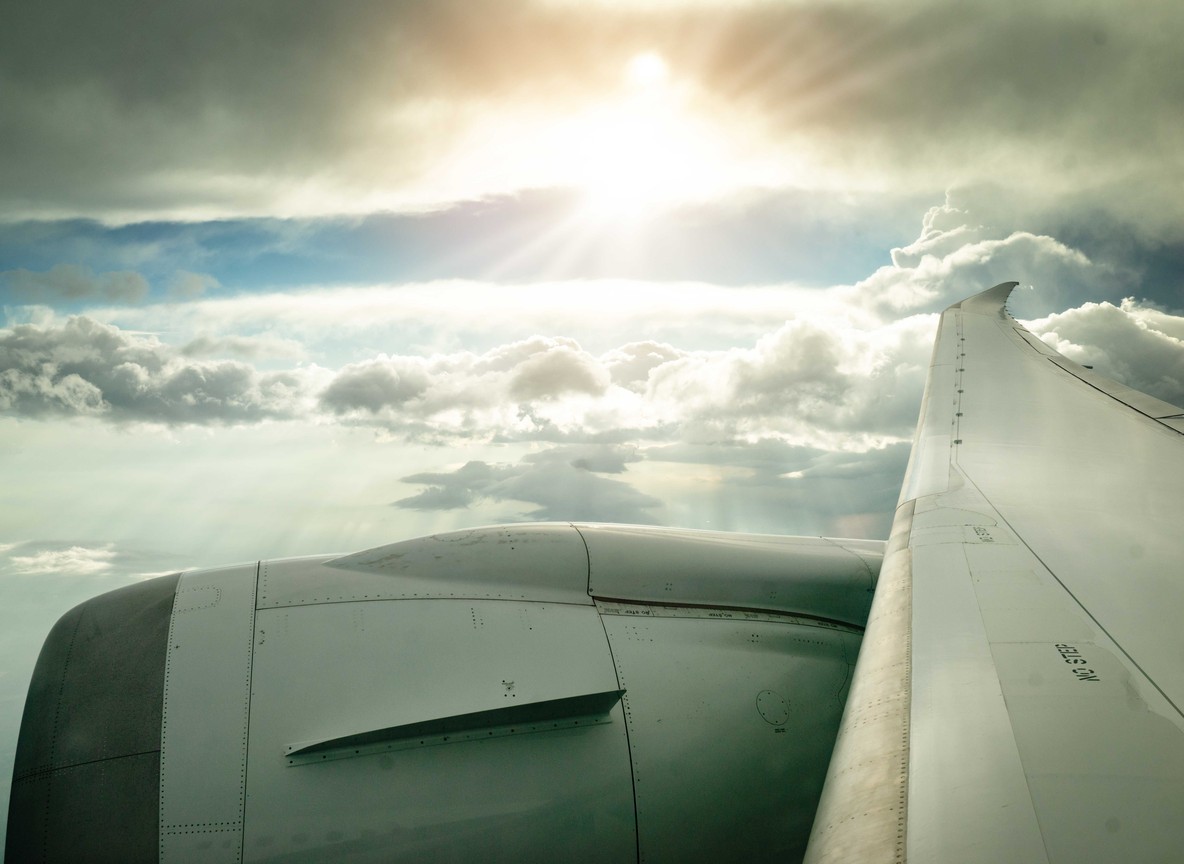 a view from a plane window of the engine and wing above clouds with sunlight breaking through