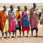 Maasai herder walking cattle across open savanna plains south of Nairobi National Park with the city skyline faint on the horizon
