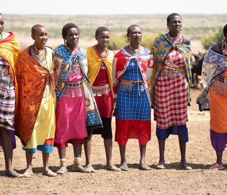 Maasai herder walking cattle across open savanna plains south of Nairobi National Park with the city skyline faint on the horizon
