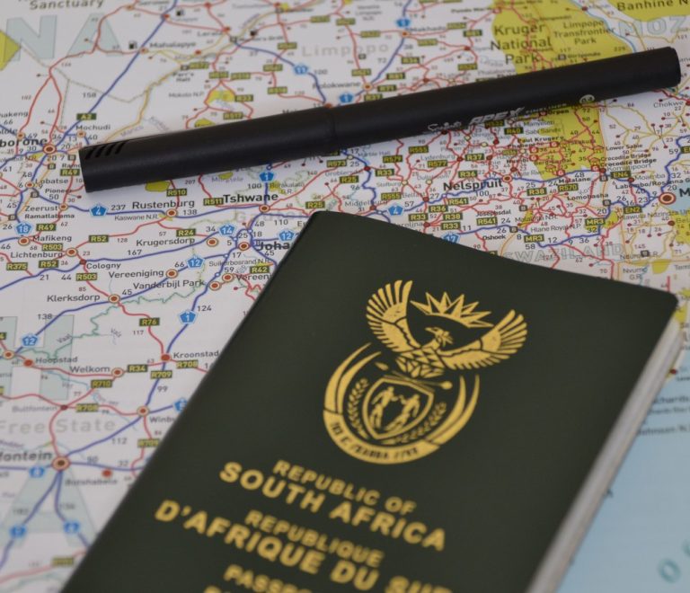 Traveler checking a laptop screen showing a travel authorization portal, passport and boarding pass on the desk beside a safari bag