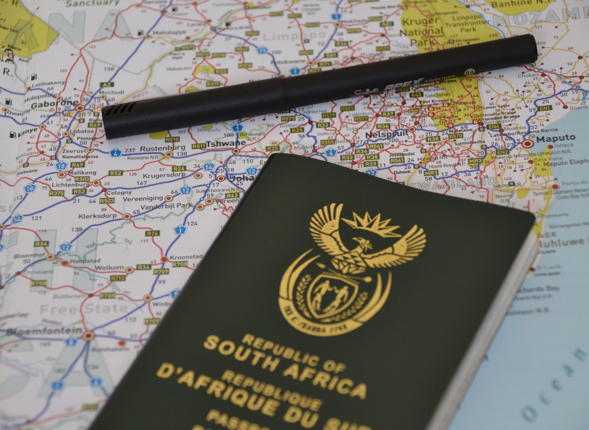 Traveler checking a laptop screen showing a travel authorization portal, passport and boarding pass on the desk beside a safari bag