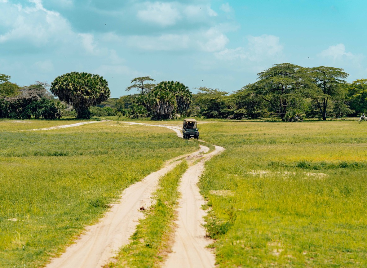 A safari vehicle following a dirt track through the bush toward camp, the kind of short transfer that links an airstrip to your next lodge