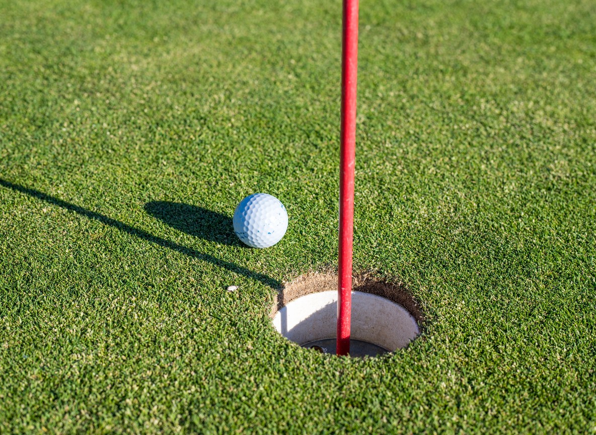 Close-up of a golf ball resting beside the hole and flag pin on a putting green