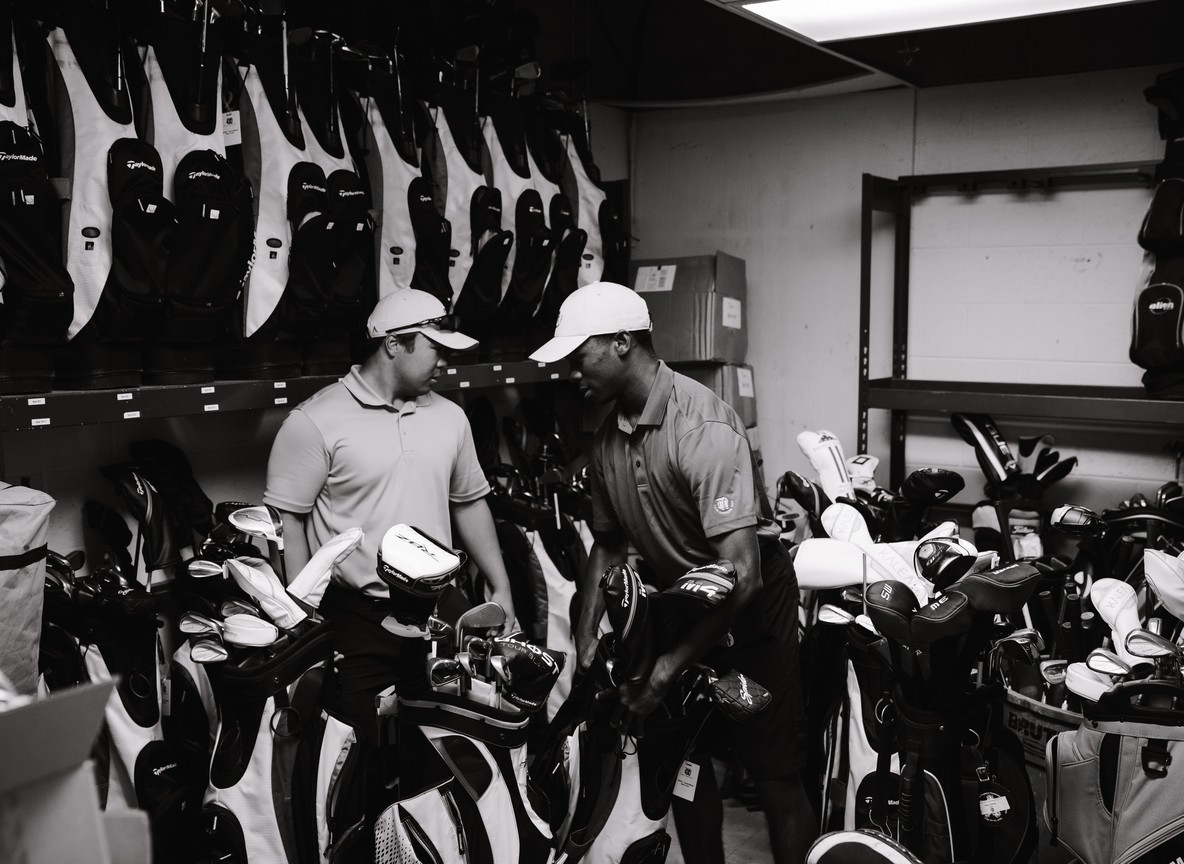 Golfers sorting rental clubs and bags in a course pro shop, the kind of rental counter travelers will find at coastal clubs