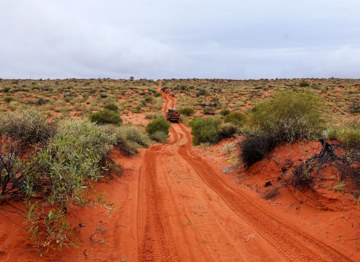 A Kenya Wildlife Service ranger on a motorbike patrol along a dry, rocky track in Turkana County, distant hills under a pale sky