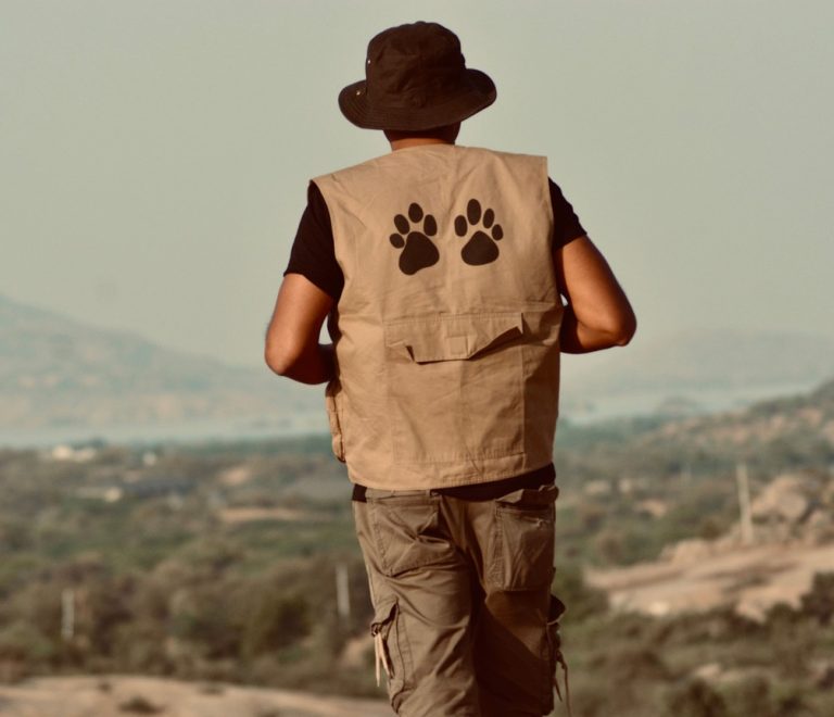 a traveler in khaki and olive safari clothing standing beside a safari vehicle in golden grassland, Maasai Mara National Reserve