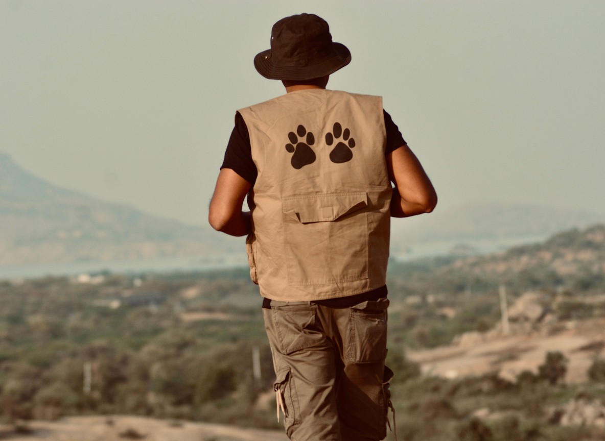 a traveler in khaki and olive safari clothing standing beside a safari vehicle in golden grassland, Maasai Mara National Reserve