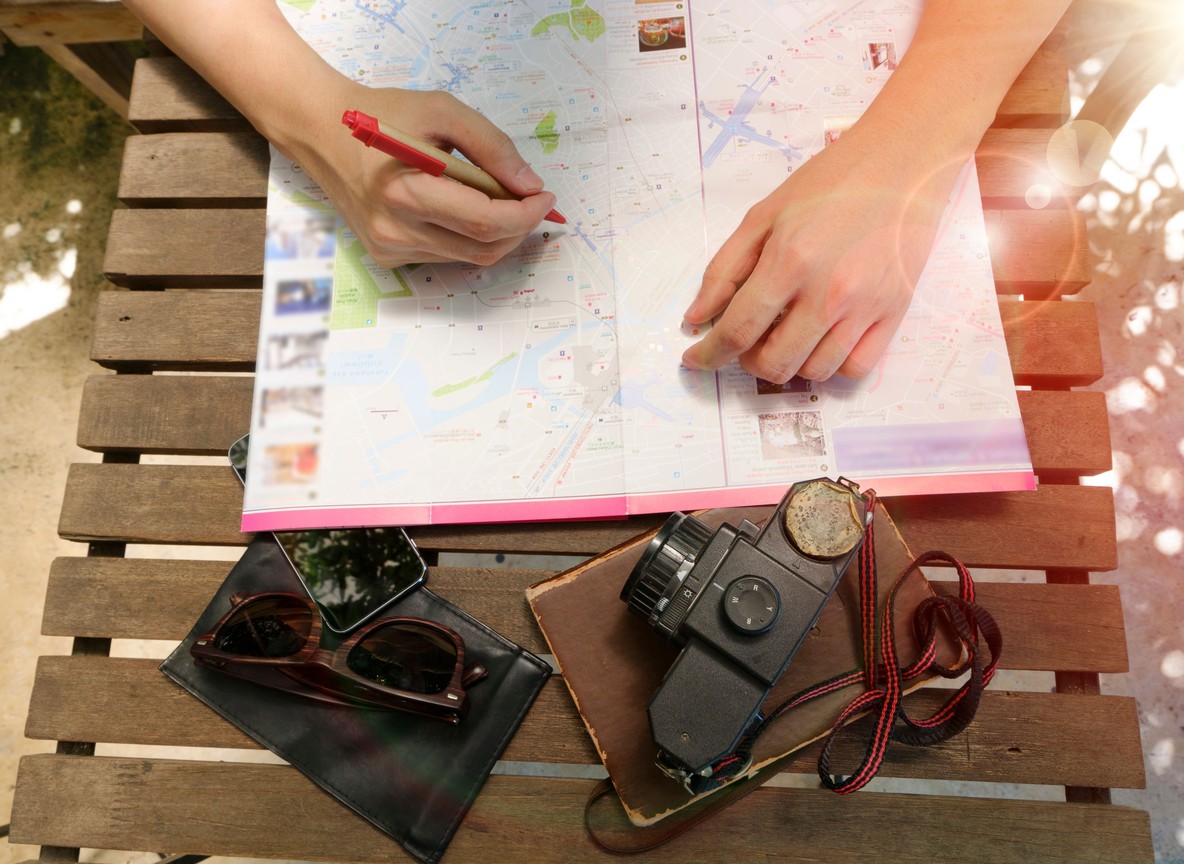 A traveler planning a safari itinerary on a map with a camera and sunglasses on a wooden table