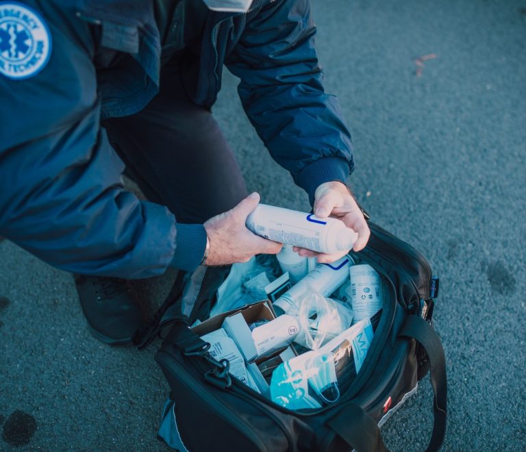 An open travel medical kit with bandages, antimalarial tablets, and insect repellent laid out on a safari camp bed with mosquito netting visible