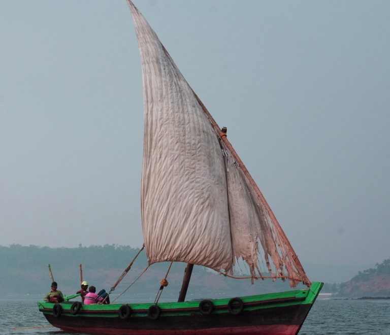 A traditional wooden dhow with a triangular sail crossing calm water off Lamu Island at sunset