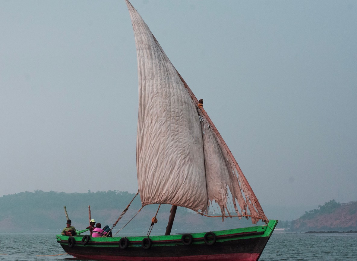 A traditional wooden dhow with a triangular sail crossing calm water off Lamu Island at sunset