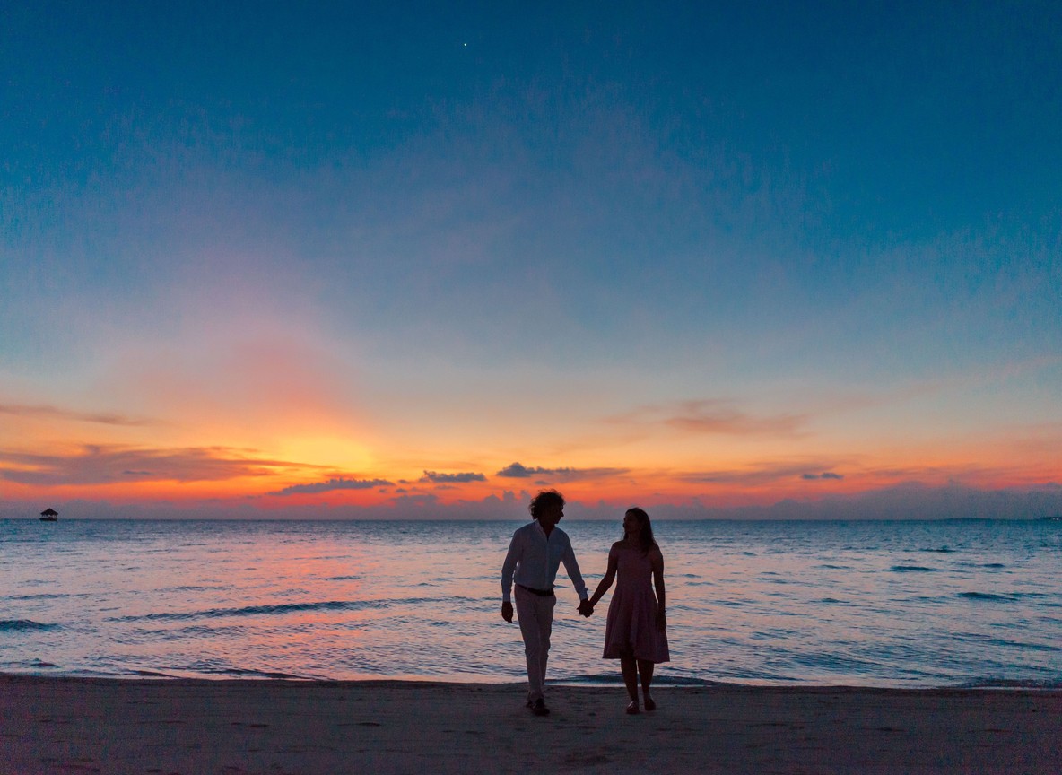 A couple holding hands and walking barefoot along the shoreline at sunset, the quiet moment that often follows a Lamu dhow sail