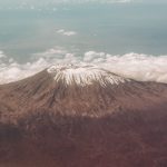 Runners on a mountain trail with Mount Kenya's peaks visible in the background at sunrise