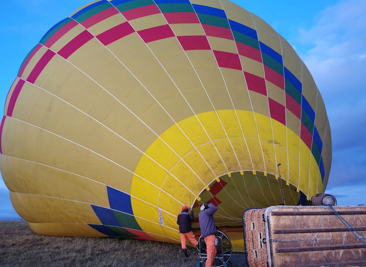 Ground crew inflating a hot air balloon basket at dawn with guests boarding in the Masai Mara
