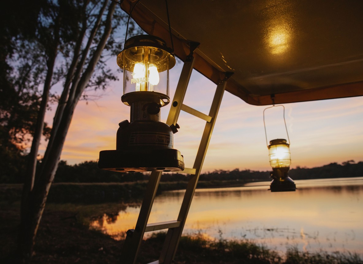 Lanterns lit at dusk outside a safari camp tent overlooking a Mara river channel