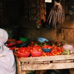 A vendor's market stall in East Africa piled with fresh tomatoes, peppers, and produce, the kind of small daily purchase mobile money covers on the road