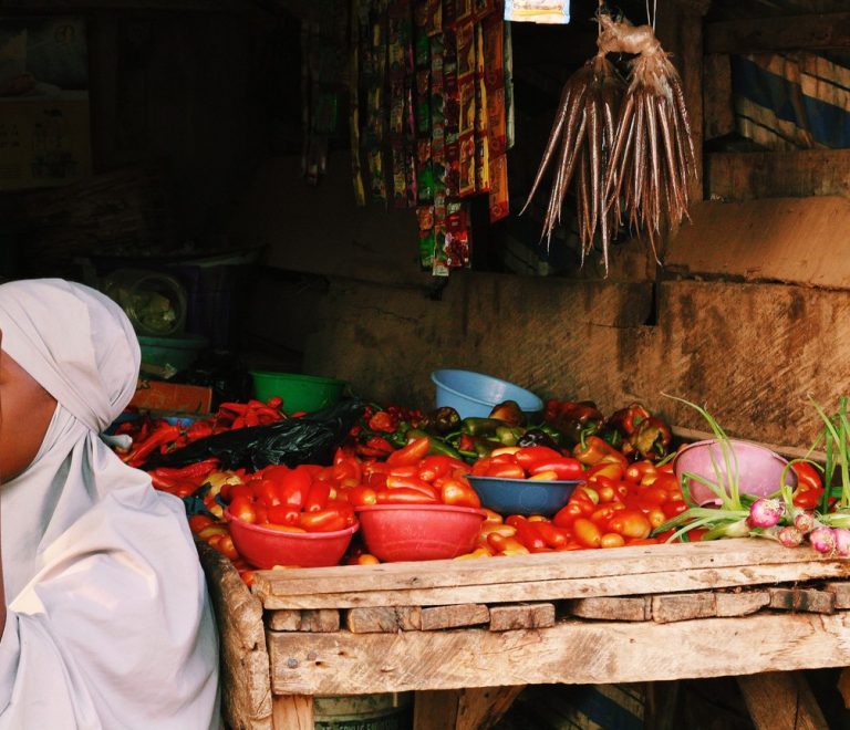 A vendor's market stall in East Africa piled with fresh tomatoes, peppers, and produce, the kind of small daily purchase mobile money covers on the road