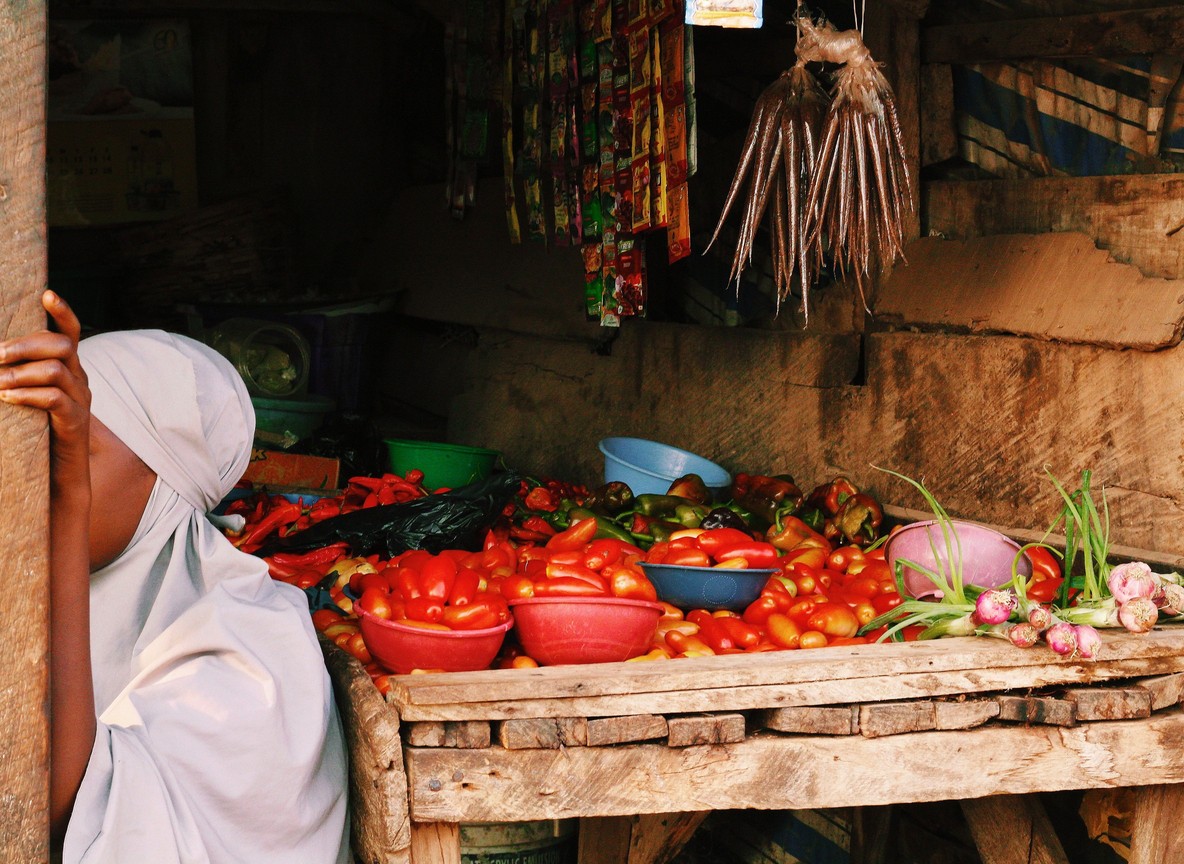 A vendor's market stall in East Africa piled with fresh tomatoes, peppers, and produce, the kind of small daily purchase mobile money covers on the road