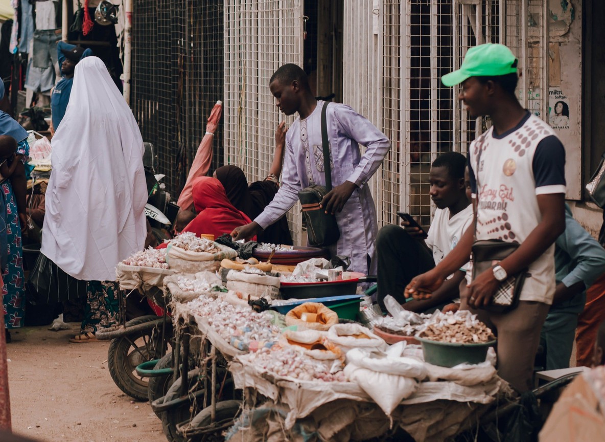 A bustling street market in an African city with small vendor stalls lining the road, the everyday setting where mobile money gets used most