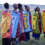 a group of Maasai women in colorful traditional shuka and beaded jewelry standing together on open grassland in Laikipia, Kenya