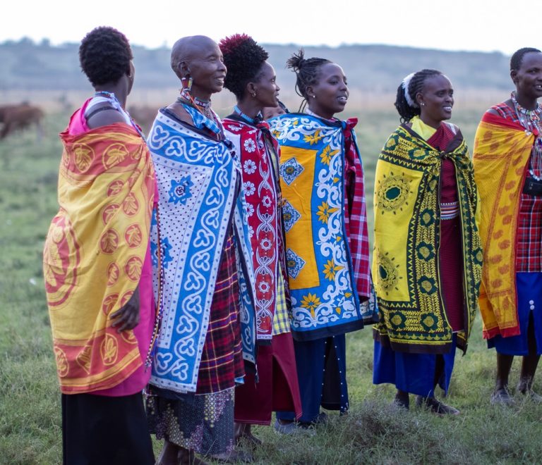 a group of Maasai women in colorful traditional shuka and beaded jewelry standing together on open grassland in Laikipia, Kenya
