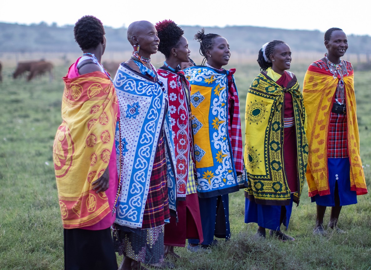 a group of Maasai women in colorful traditional shuka and beaded jewelry standing together on open grassland in Laikipia, Kenya