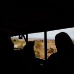 A single open safari vehicle parked on an empty savannah track at golden hour with no other vehicles in sight, Laikipia hills in the background