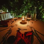 a candlelit table set under acacia trees on the savanna at dusk, lanterns and a couple silhouetted against an orange sky