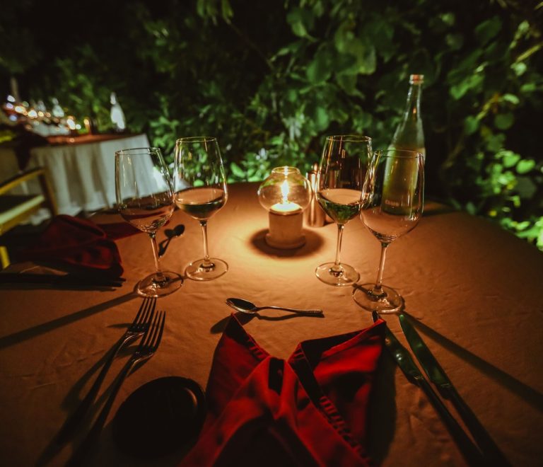 a candlelit table set under acacia trees on the savanna at dusk, lanterns and a couple silhouetted against an orange sky