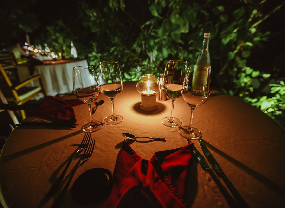 a candlelit table set under acacia trees on the savanna at dusk, lanterns and a couple silhouetted against an orange sky