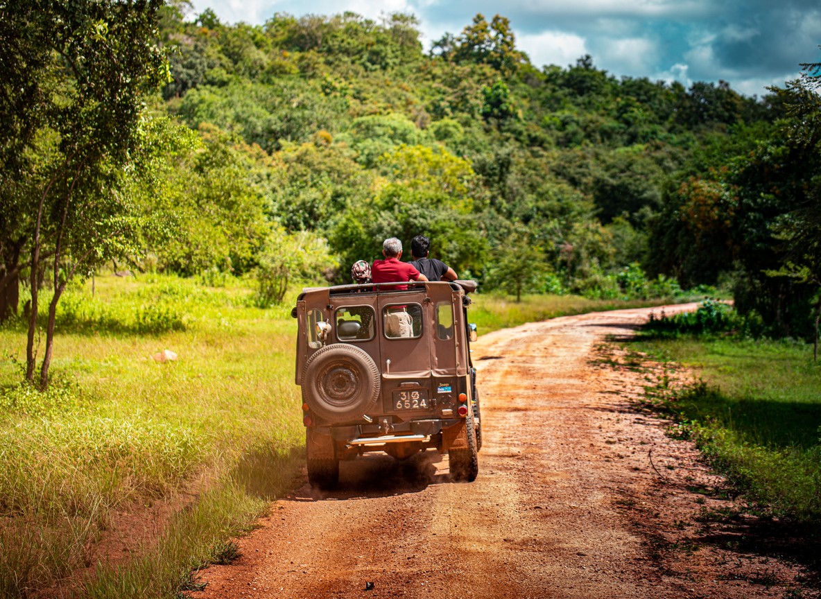 Safari travelers riding an open 4x4 vehicle along a dirt track in Kenya