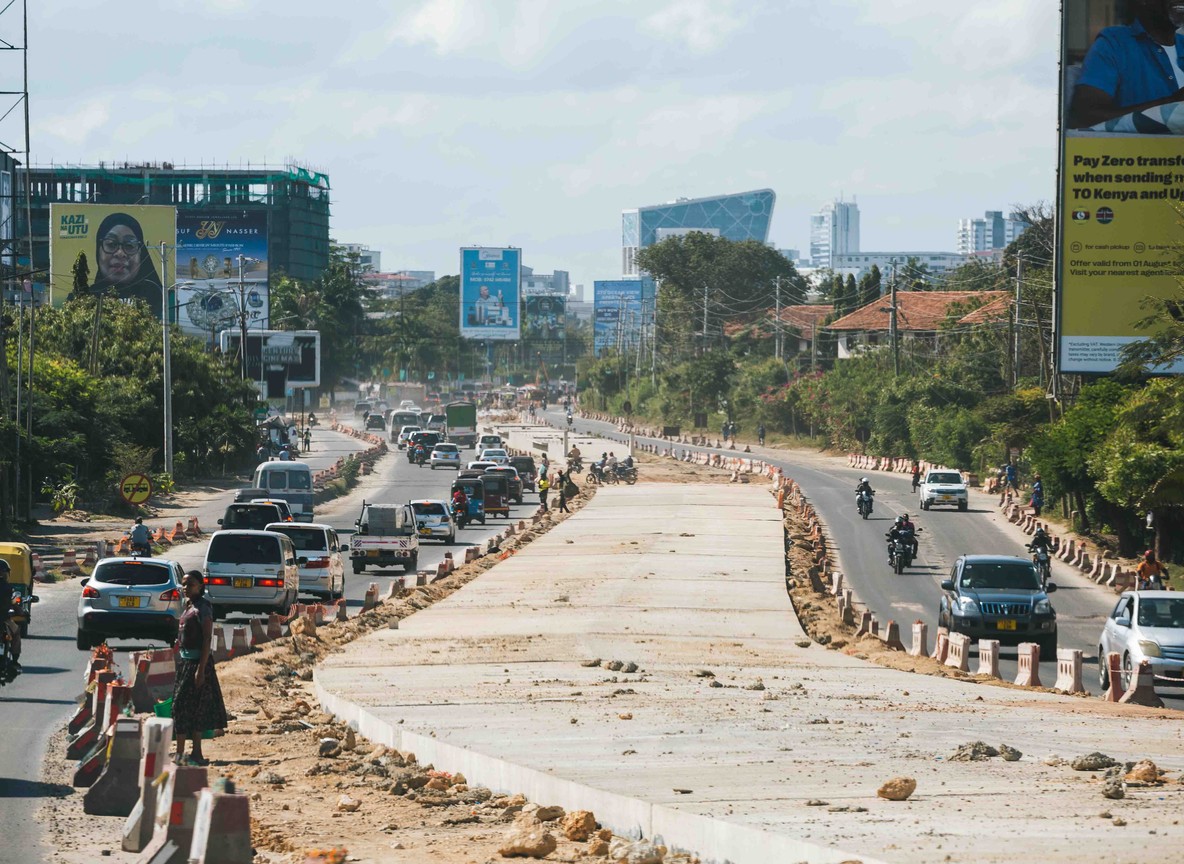Road construction equipment and a graded dirt track cutting through Serengeti savanna near the western corridor