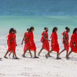 a line of newly graduated community scouts in field uniform standing at attention on dry red earth with the Chyulu Hills faint in the background