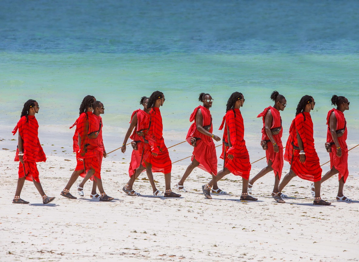 a line of newly graduated community scouts in field uniform standing at attention on dry red earth with the Chyulu Hills faint in the background